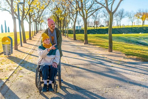 Happy friends enjoying a sunny autumn day together outdoors in a park, one pushing a wheelchair and