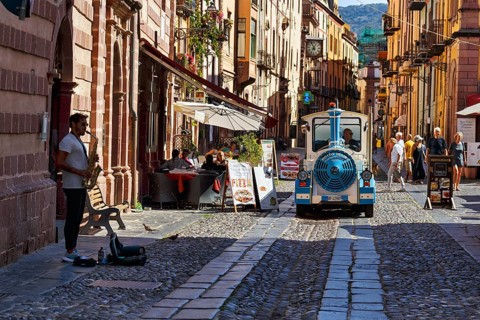 Trolleybus, street musicians, pedestrians and tourists in the picturesque old town of Bosa,