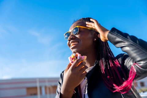 Low angle view photo of an african woman eating a multicolored doughnut in the street