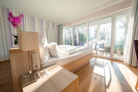 Modern, bright bedroom with wooden floor, large windows and a purple flower on the bedside table,