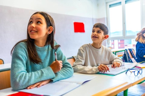 Two young pupils listening to their teacher in elementary school classroom during lesson, education