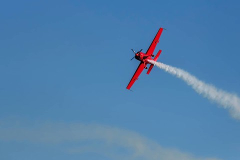 Red stunt aerobatic plane performing stunts in blue sky. Concept of speed, difficulty, precision,