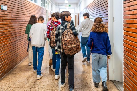 Group of elementary school students walking down school hallway between classes, carrying backpacks