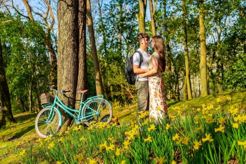 Romantic couple hugging in a forest full of daffodils with a bicycle parked nearby, enjoying a