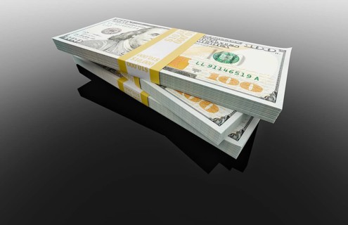Stack of thirty thousand dollars of one hundred dollar bills on black reflective surface.