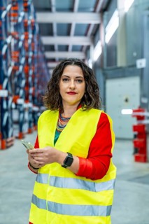Vertical portrait of a female manager of warehouse wearing safety reflective clothes using mobile