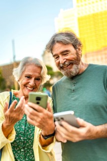 Vertical close-up photo of a caucasian happy modern senior couple using smartphone in the city