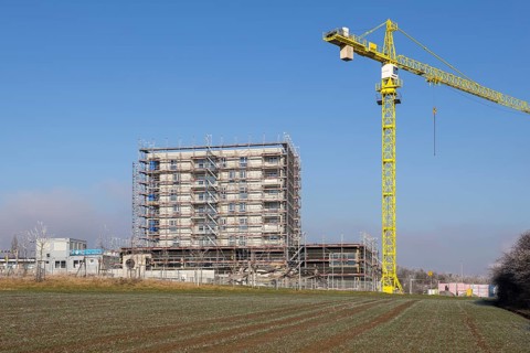 Unfinished building with yellow construction crane, construction site under blue sky, housing