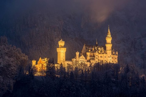 An enchantingly illuminated castle towers over a snow-covered mountain forest, Neuschwanstein,