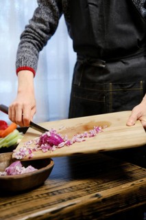 Unrecognizable man puts chopped red onions from a wooden cutting board in wooden bowl in the