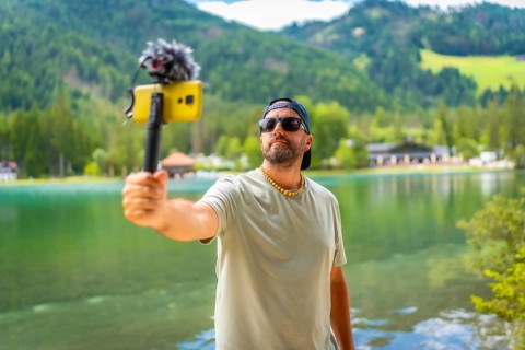Content creator filming a video with a smartphone and external microphone at lake dobbiaco in the