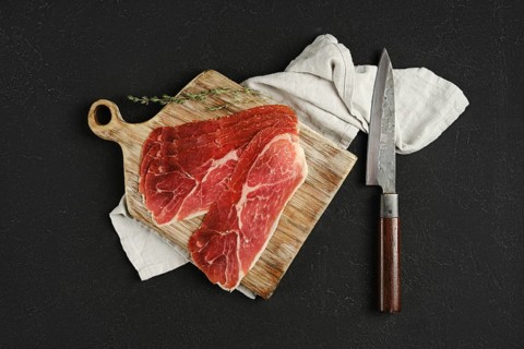 Overhead view of jamon iberico cured pork meat on a wooden cutting board, accompanied by a sharp