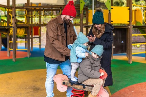 Parents watching their children joyfully riding a spring rider on a colorful playground, creating