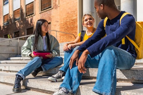 Multi-ethnic friends sitting on the stairs of the university talking together relaxed