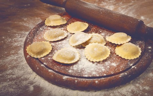 Fresh raw, uncooked ravioli, on a cutting board, with a rolling pin for dough, wooden background,