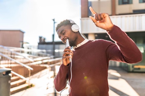 African man dancing listening to music with headphones in the city in a sunny day of autumn