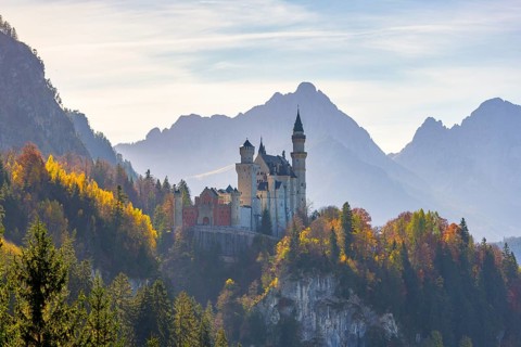 Romantic castle enthroned in autumnal forests against a mountain backdrop, Neuschwanstein,