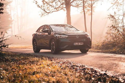 A Volkswagen on a country road in the morning sun mist between autumnal trees, electric car VW ID5,