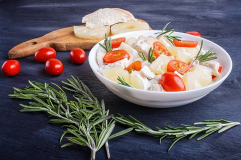 Chicken fillet salad with rosemary, pineapple and cherry tomatoes on dark blue wooden background.