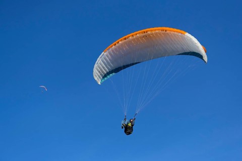 Paraglider with orange wing flies freely under a clear blue sky
