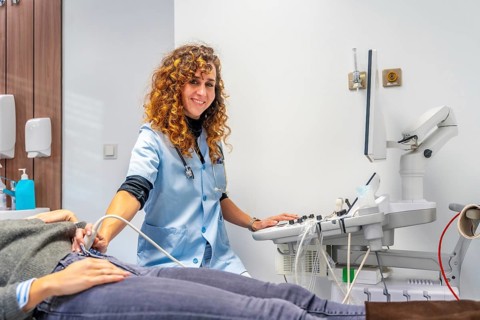 Female doctor smiling at camera while performing an ultrasound to a pregnant woman into the
