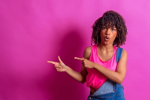 Surprised young woman with curly hair points to the side with a shocked expression, suggesting a