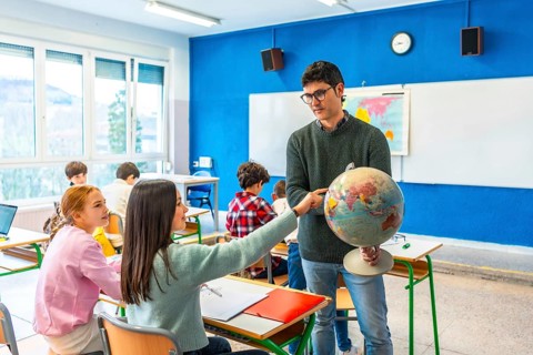 Geography teacher engaging students by pointing out countries on a globe during an interactive
