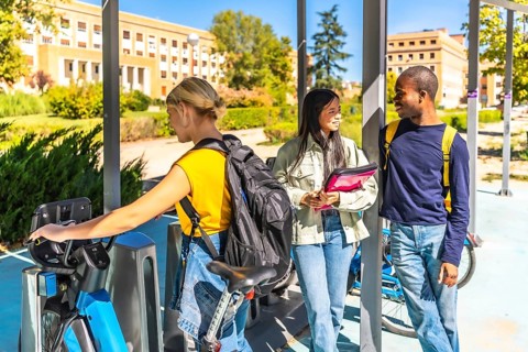 Student choosing bike in a public bicycle service area next to multi-ethnic friends
