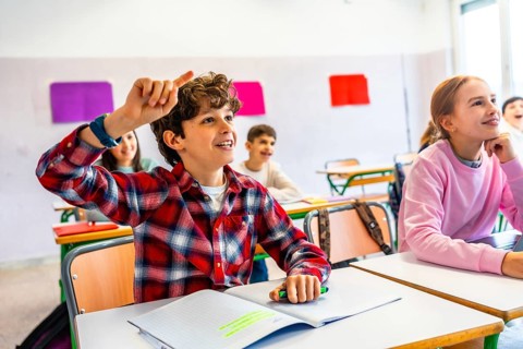 Elementary school student raising hand to answer a question during class, showing eagerness to