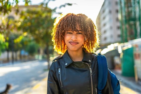 Confident young latin woman with curly hair and leather jacket smiling at camera standing in the