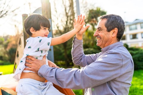 Grandfather and grandson are enjoying time together at the playground, giving a high five and