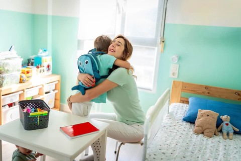 Tender mother embracing her son before going to school sitting on the kids bedroom