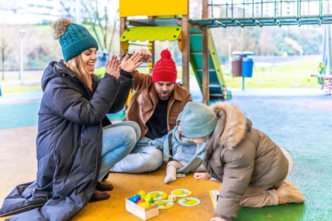 Parents and children having fun together playing a board game on a playground during winter