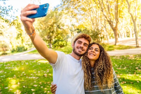 Frontal view of a young caucasian couple taking selfie standing in a park in a sunny day of spring