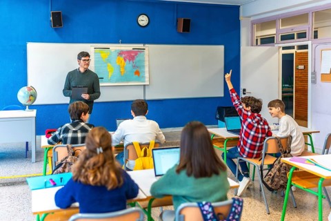 Group of teenage students raising hand and following geography lesson in classroom with teacher and