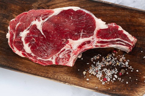 Raw rib eye steak, cowboy steak, wooden chopping board, marble table, top view, no people