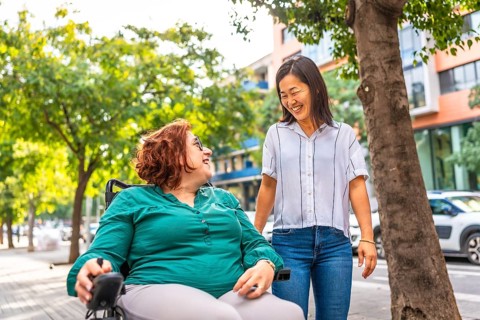 Asian woman and friend with disability talking and walking along a residential street