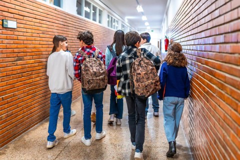 Rear view of diverse group of students walking down school hallway between classes, carrying