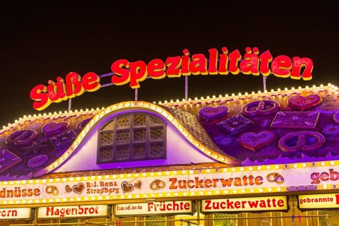 Candy stall flooded with light at a funfair at night, decorated with traditional treats,