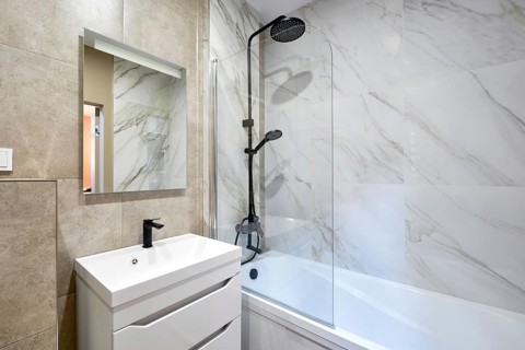 A beautifully designed bathroom showcases marble walls and a stylish shower-bathtub combo. A modern