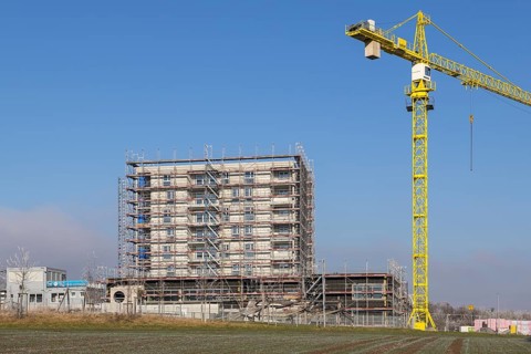 Incomplete building with yellow construction crane in clear sky, housing construction, new