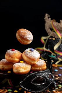 Berliners, doughnuts with icing sugar and Smarties next to a black mask, carnival