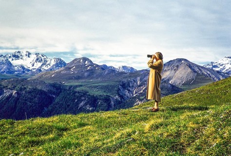Woman standing on hillside using binoculars in mountains of national park, Western Rhaetian Alps,