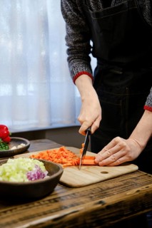 Unrecognizable man is chopping vibrant carrots on a wooden cutting board while surrounded by fresh