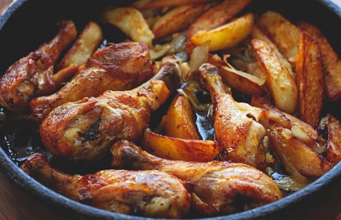 Fried chicken drumsticks with potato slices, in a clay pan, baked in the oven, with spices,