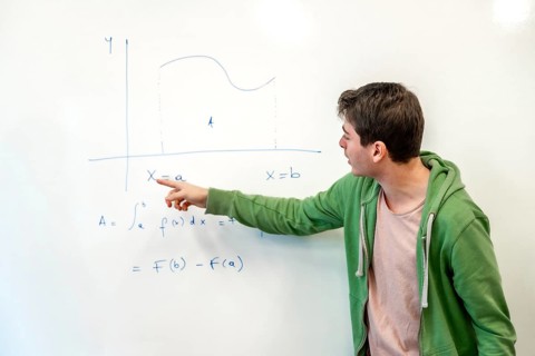 Young college student explaining a mathematical integral calculus formula, pointing at a graph on a