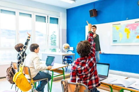 Group of elementary school students raising hands to answer teacher's question in geography class