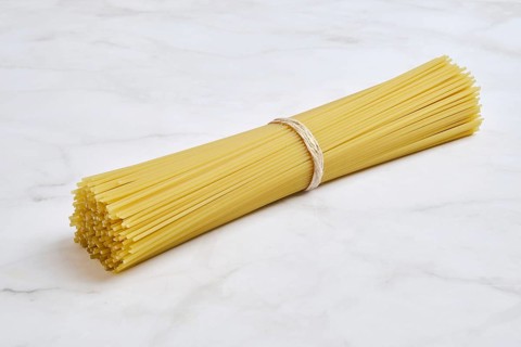 A tightly bound bundle of uncooked spaghetti on a smooth light marble surface