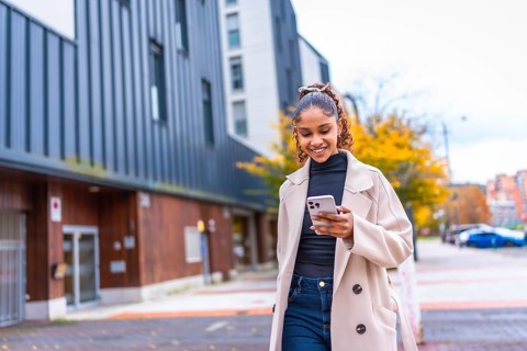 Happy stylish african american young woman using phone walking in the city in autumn