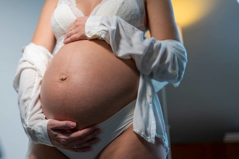 Close-up of a pregnant woman in white underwear holding her belly